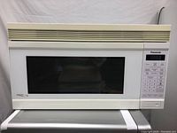 Front view of a white Panasonic over-the-range microwave oven showing the large black viewing window, control panel on the right with multiple buttons and digital display, and top vent grills.