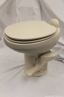 Side view of the portable toilet showing the pedal flush on the right side and closed lid with smooth ivory finish.