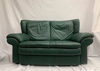Front-facing view of the green leather loveseat with plush cushions and wide armrests against a white backdrop.