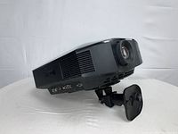 Black Sony projector on white fabric backdrop showing front lens and side vents, mounted on adjustable bracket