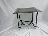 Photo of one square glass and metal accent table showing clear tempered glass top and black metal legs with circular detail near base.