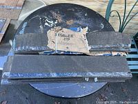 Two black starter shingle strips stacked on a round black metal table, showing packaging remnants and tactile granulated surface texture.