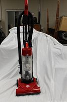 Red Dirt Devil Quick Lite upright vacuum standing upright showing clear dirt cup, handle, hose and brush head.