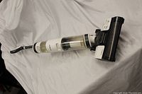 Full length photo of the Tineco cordless vacuum cleaner showing the motorized brush head, dustbin, and ergonomic handle on a white fabric background.