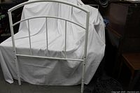 Photo of white metal headboard showing arched design and vertical slats against white sheet background