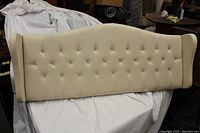 Full front view of the light beige upholstered headboard showing diamond tufted pattern, curved top and wingback sides.