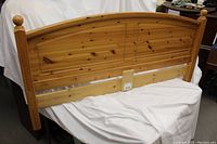 Photo of wooden pine headboard with gently curved top and rounded finials on posts, showing wood grain and knots.