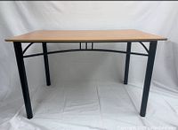 Front view of the table showing the natural woodgrain laminate surface and black metal frame with curved accents.