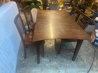 Full view of rectangular wooden dining table with dark finish and four matching chairs with slatted backs. Table shows signs of use and wear.