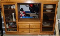 Full front view of solid oak wooden entertainment center showing two glass-front cabinets with shelving, four drawers in the center, and open space in middle section for TV or media equipment.