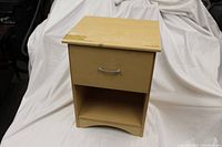 Front view of wooden nightstand showing drawer and open shelf below, with chips and wear on top surface.