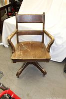 Front view of vintage wooden office chair showing curved armrests, seat with visible wear, and swivel base with casters.