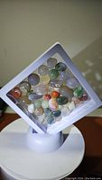 Cube-shaped white float display holding multiple polished natural agate stones of various colors and patterns