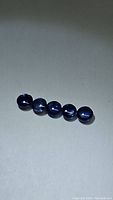 Five round cabochon cut natural blue sapphires displayed on a flat surface showing their denim blue color and rounded shape.