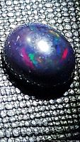 Close-up image of the oval black opal cabochon showing its multicolored play-of-color on a textured black background.