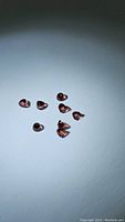 Eight small orange-red garnet stones with a polished fancy bullet cut shape shown on white background.