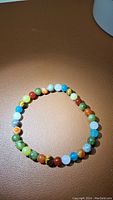 Front view of the mixed gemstone beaded stretchy bracelet showing multicolored round beads including green, blue, yellow, orange, brown, and white on an elastic band.