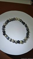 Photo of natural black web jasper stretchy bracelet arranged on white surface showing round black, white, and grey jasper beads with natural web pattern variations.