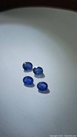 Four oval cut natural blue sapphires arranged on a white surface, showing uniform deep blue color and faceting.