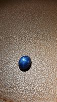 Close-up image of oval blue star sapphire cabochon on textured surface, showing star effect