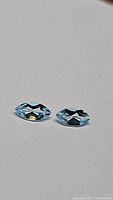 Two natural marquis cut sky blue topaz gemstones shown from an angle on grey surface.