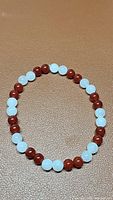 Front angle shot of the elastic bracelet showing alternating 6mm red Carnelian and white Jade beads on a brown surface.