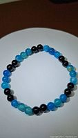 Photo of a circular bead bracelet made with alternating ocean blue agate and black onyx beads laid flat on a white surface.