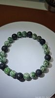 Photo from above showing natural black lava stone beads alternating with green spotted jasper beads, laid flat to display full circular bracelet