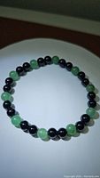 Photo of stretchy gemstone bracelet laid flat showing alternating green aventurine and black onyx round beads of about 6mm size.
