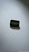 Close-up photo of natural green tourmaline octagon cut gemstone on white background showing facets and color