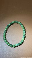 Natural green jade bead stretchy bracelet laid flat on a brown surface showing the uniform 6mm round beads.