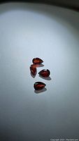 Four pear cut garnet gemstones with a deep cherry red color displayed on a light surface under direct lighting, highlighting their clarity and shape.