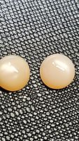 Close-up photo of two round peach moonstone cabochon gemstones on a textured black background, showing smooth polished surfaces and light reflections.
