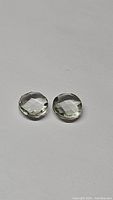 Pair of faceted, round prasiolite green amethyst gemstones placed on a plain white background showing their light green color and clarity.