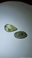 Two natural mossy green prehnite cabochons, one pear-shaped and one oval-shaped, on white background.