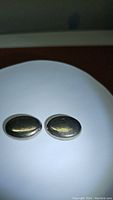 Photo of a matched pair of oval natural pyrite cabochon stones with golden platinum color on white background showing reflective surfaces.