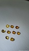 Photo showing ten round cut yellow to orange sapphires under direct light on white background, highlighting color and clarity.
