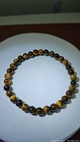 Photo of a natural tigerseye beaded bracelet laid flat on a white surface showing the round polished brown and yellow beads.