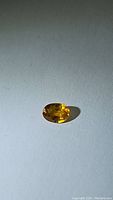 Clear image of an oval cut natural yellow sapphire on white background showing depth of color and clarity.