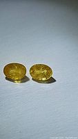 Two oval yellow sapphires with visible internal inclusions, polished surface, placed on white background for size and color visibility.