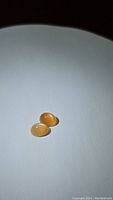 Two oval peach moonstone cabochons placed on a white surface under bright light. The stones show a smooth polished surface and a warm peach tone.