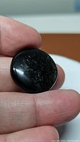 Photo showing a round black obsidian cabochon with reflective silver sheen held between fingers
