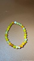 Yellow agate stretchy bracelet laid flat on brown surface showing round beads in multiple shades of yellow and complementary colors.