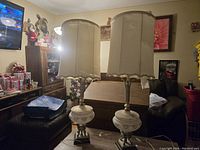 Two large lamps with deteriorating shades placed on a table in a room with furniture and decorations visible in the background.
