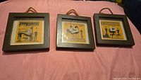 Three small square framed pictures with Egyptian art, hanging on a pink surface