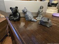 Four figurines arranged on a surface: bear cub, raccoon, human figure, toad.
