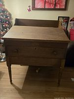 Front view of antique wooden secretary desk showing slant front, drawer with two knobs and turned legs, with some visible wear.