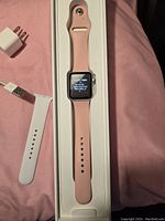 Apple Watch Series 3 with pink band in original white box, powered on showing Japanese language screen.