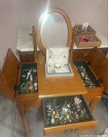 Full view of wood standing jewelry box on legs with marble top, mirror, compartments open and drawers filled with assorted jewelry