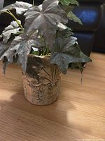 Front angle showing artificial plant leaves and decorative planter with embossed leafy and scroll designs.